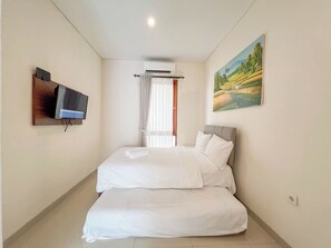 A hotel room with a bed, a television mounted on the wall, an air conditioning unit, and a painting on the wall. - 3BR Casa De Uli Villa Near GWK (Nusa Dua)