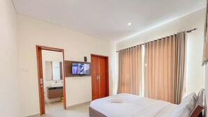 Habitación de hotel con cama, televisor montado en la pared, baño con lavamanos y puerta que da a otra habitación.