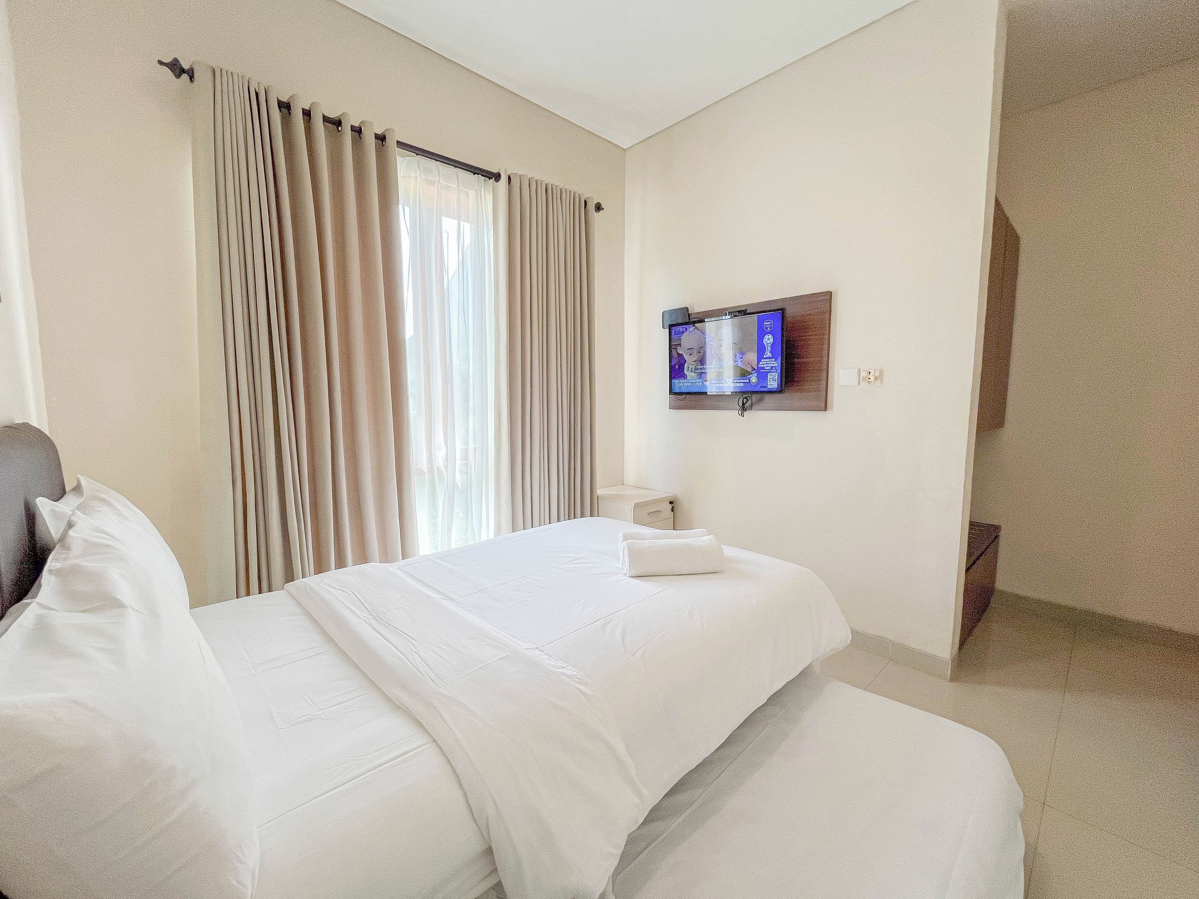 Een hotelkamer met een bed, gordijnen, een aan de muur bevestigde televisie en een klein nachtkastje.