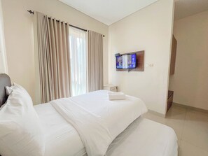 A hotel room with a bed, curtains, a television mounted on the wall, and a small bedside table. - 3BR Casa De Uli Villa Near GWK (Nusa Dua)