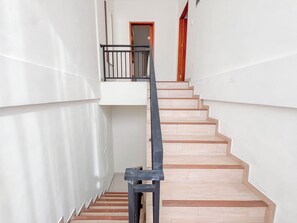 Een trap met houten treden en een metalen leuning, die uitkomt op een vloer met een deur.
