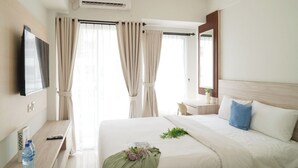 Ein Hotelzimmer mit Bett, Nachttisch, Fernseher, einem Fenster mit Vorhängen, einem Spiegel und einer Klimaanlage.