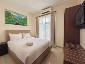 A hotel room with a large bed, a painting on the wall, an air conditioning unit, and a television mounted on the wall. - 3BR Jimbaran Villa at Casa De Uli Bali (Jimbaran)