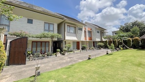 A modern residential building with a paved driveway, a well-maintained lawn, and a variety of potted plants and shrubs. - Spacious And Homey 3Br At Villa Casa De Uli (Jimbaran)