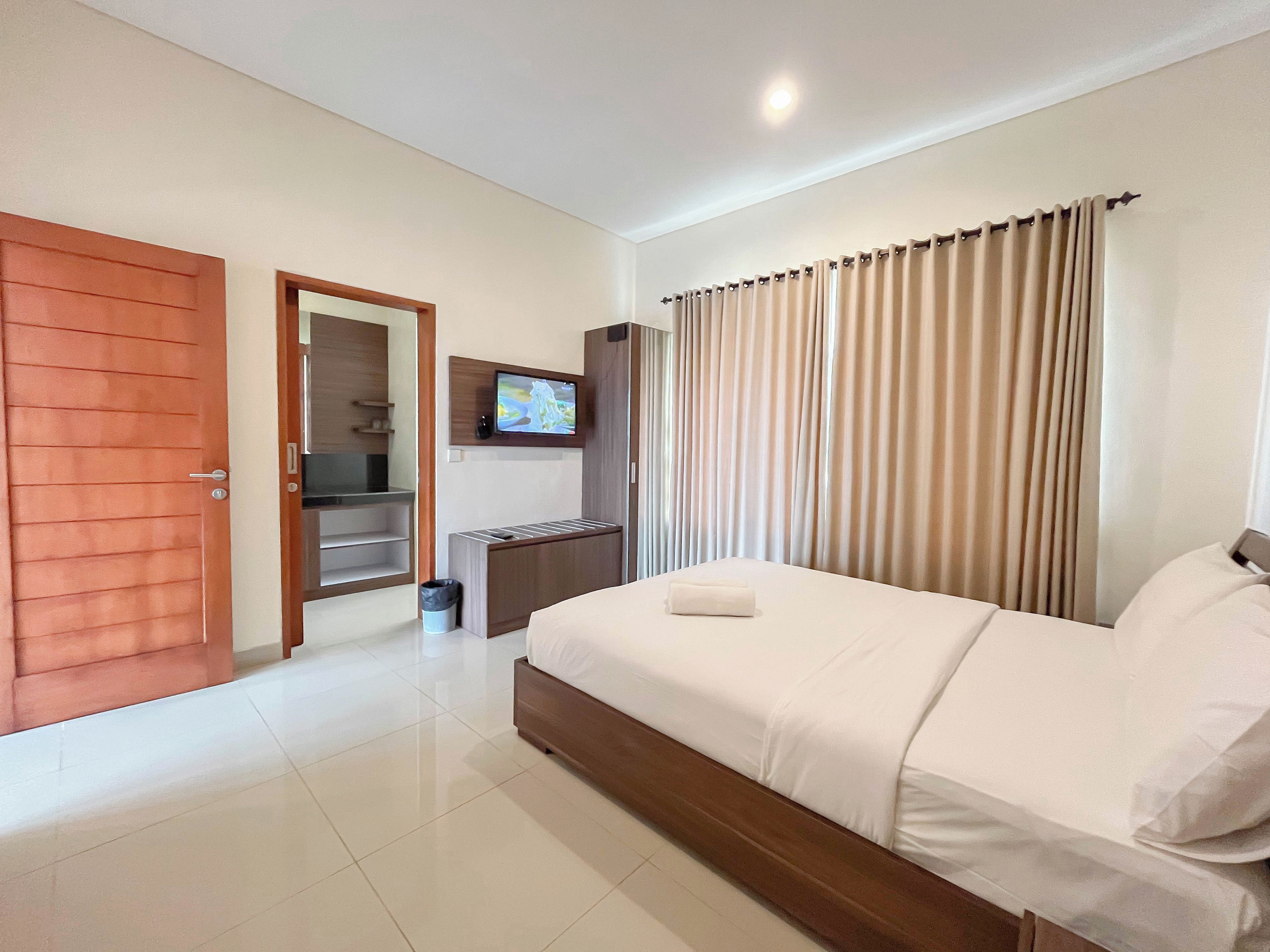 A hotel room with a bed, a TV mounted on the wall, a wooden door, and a window with curtains.