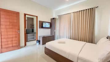 A hotel room with a bed, a TV mounted on the wall, a wooden door, and a window with curtains.