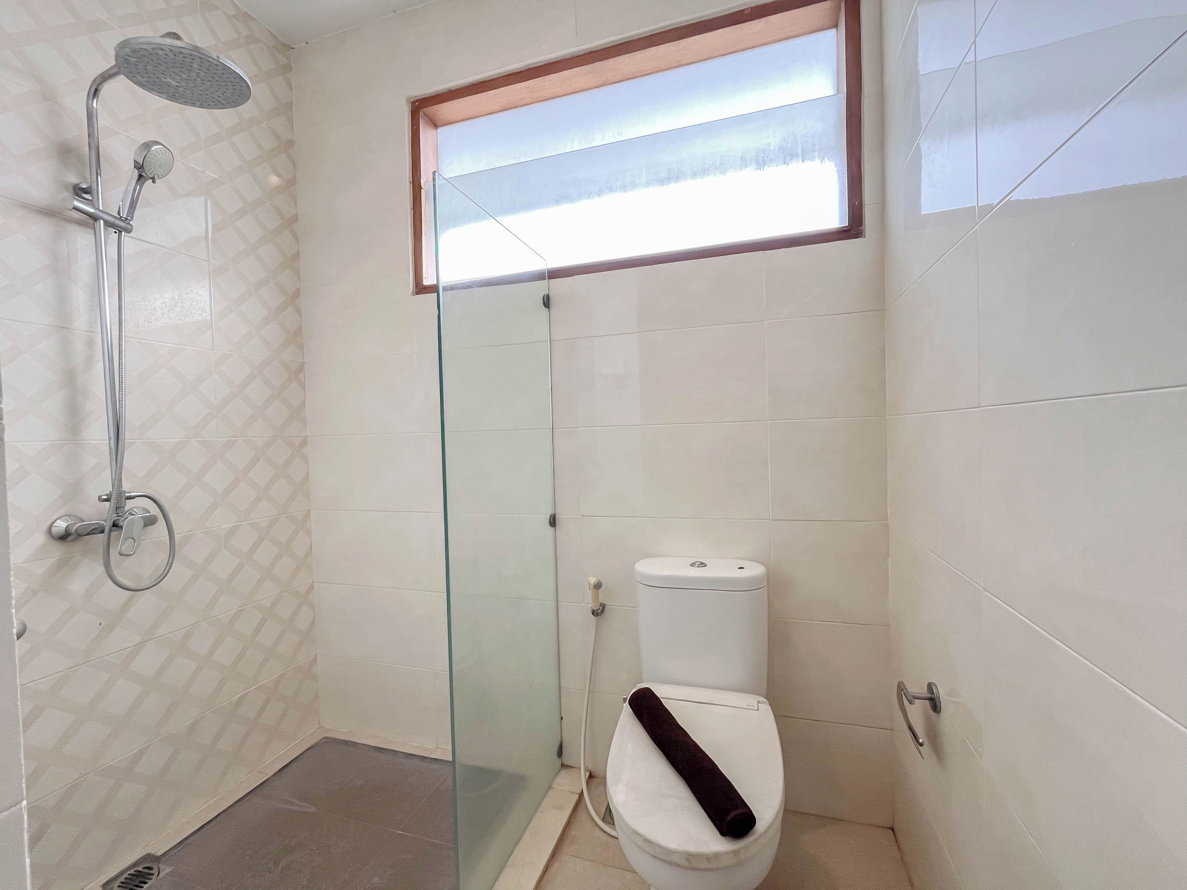 A bathroom with a glass shower enclosure, a toilet with a towel on the seat, and a window above the toilet.
