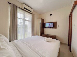 A hotel room with a bed, a TV mounted on the wall, an air conditioning unit, and a window with curtains. - 3BR Jimbaran Villa at Casa De Uli Bali (Jimbaran)