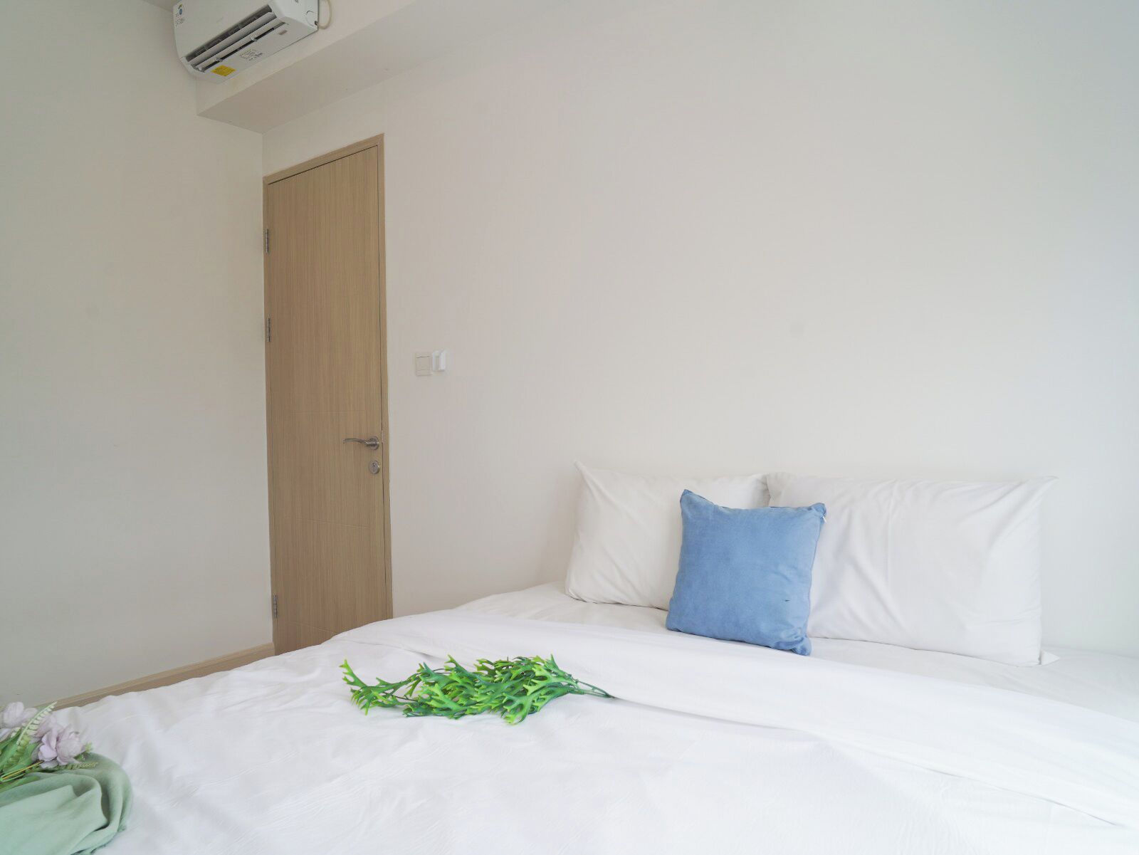 A simple, clean room with a bed, a wooden door, and a wall-mounted air conditioner.