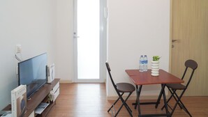 A room with a TV, a wooden table with chairs, a door, and a small plant.