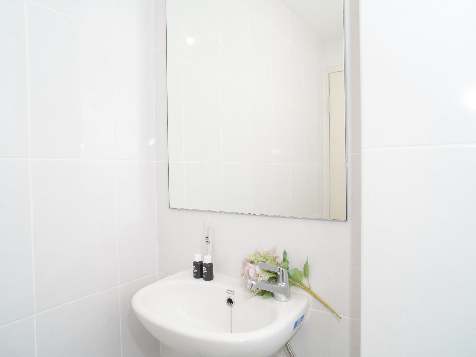 Ein helles Badezimmer mit Waschbecken, Spiegel und zwei kleinen Flaschen auf der Ablagefläche.
