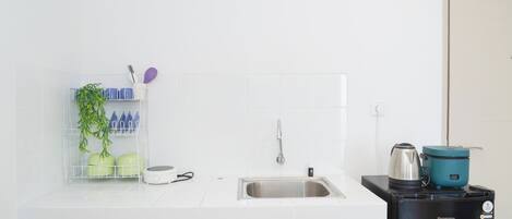 Una cocina con encimera blanca, pileta de acero inoxidable y cafetera negra.
