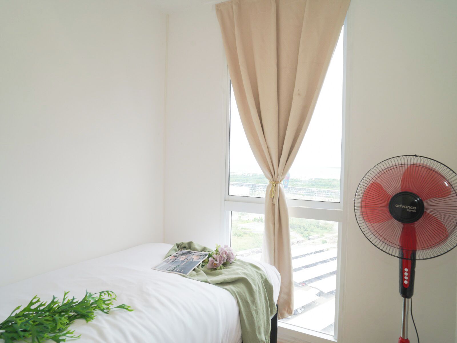 A room with a bed, a window with curtains, a fan, and a view of a bridge.