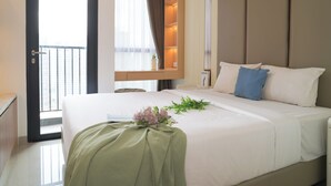 A hotel room with a bed, a desk, a chair, a window with curtains, and a door. - Chic And Comfortable Studio At Apartment Ciputra World 2 (Jakarta)