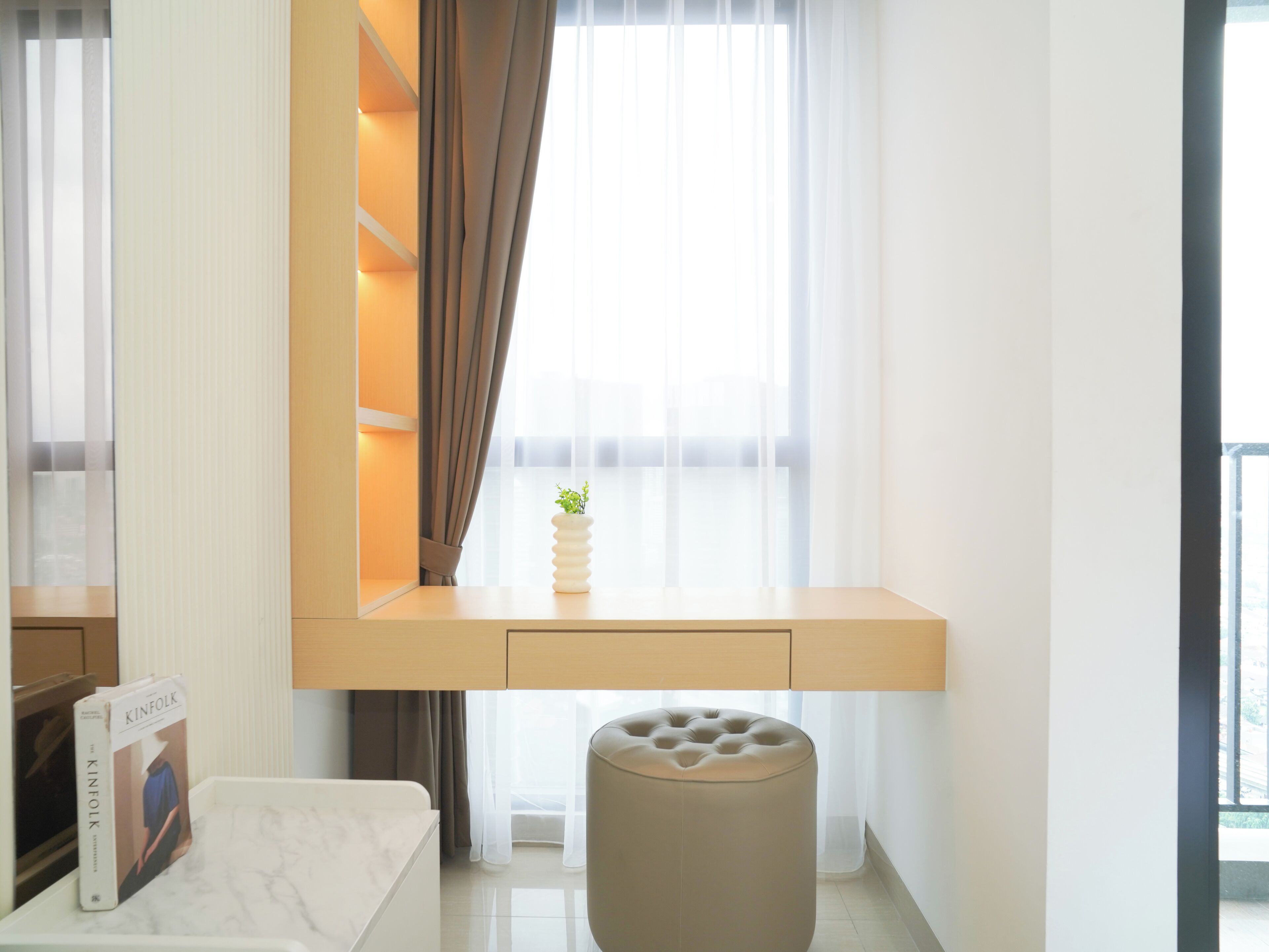 A modern room with a built-in desk, a cushioned bench, a small potted plant, and a bookshelf.