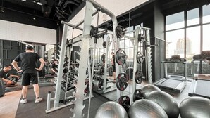 A gym with various exercise equipment, including weight machines and free weights. - Modern Brown Toned Studio At Ciputra World 2 Apartment (Jakarta)