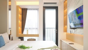 A hotel room with a bed, a TV mounted on the wall, a window with curtains, and a door. - Modern Brown Toned Studio At Ciputra World 2 Apartment (Jakarta)