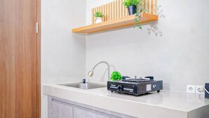 A modern kitchen with a white countertop, a stainless steel sink, a gas stove, and a wooden shelf above the sink with potted plants. - Contemporary And Cozy Studio Apartment Lrt City Sentul - Royal Sentul Park (Bogor)