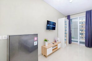 Egy modern apartman, melyben a falra szerelt, síkképernyős televízió, a beépített hűtőszekrény, egy növényt tartalmazó, fából készült szekrény, valamint egy tolóüveges ajtó vezet a balkonra.