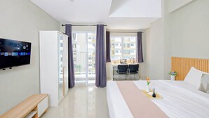 A modern hotel room with a bed, a desk, a television, and a sliding door to a balcony. - Contemporary And Cozy Studio Apartment Lrt City Sentul - Royal Sentul Park (Bogor)