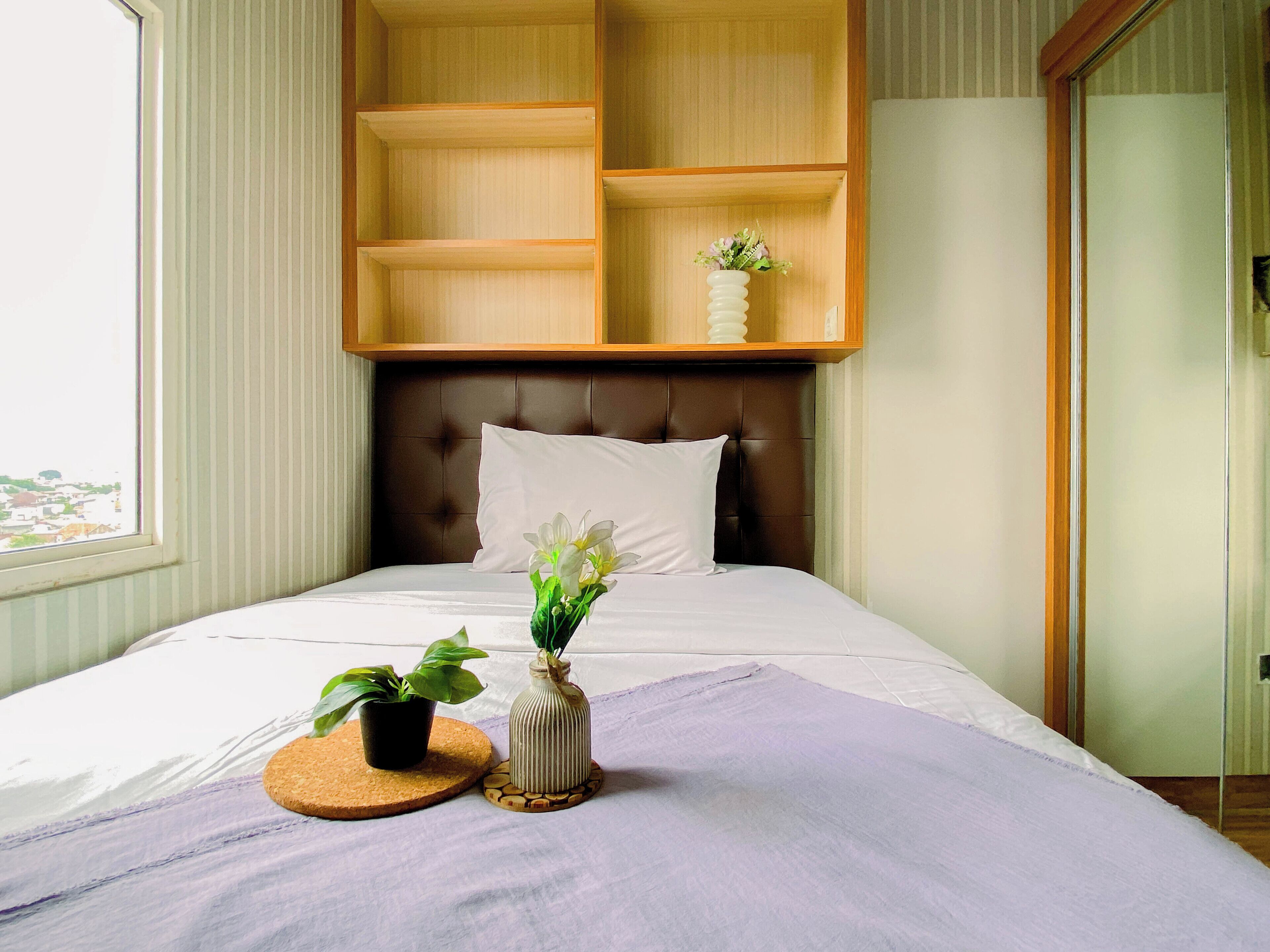 A neatly made bed with a headboard, a small potted plant, a decorative vase, and a round coaster on the bed.