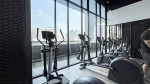 Un gimnasio con equipo de ejercicio y ventanas amplias que ofrecen vistas a la ciudad.