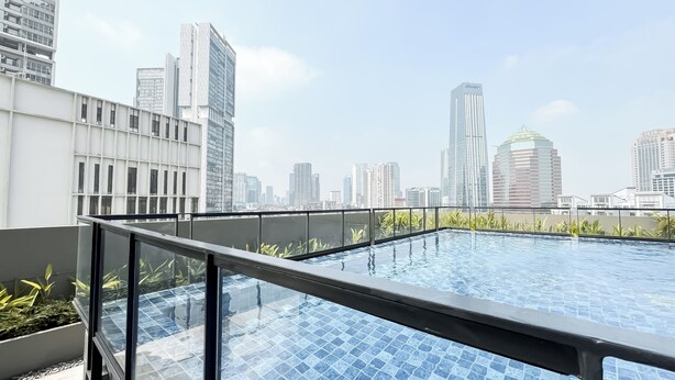 Una piscina en la azotea con vistas a un horizonte urbano, rodeada de edificios modernos.