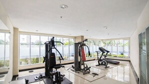 Un gimnasio con máquinas de cardio, equipo de levantamiento de pesas y un amplio ventanal con vista a un cuerpo de agua.