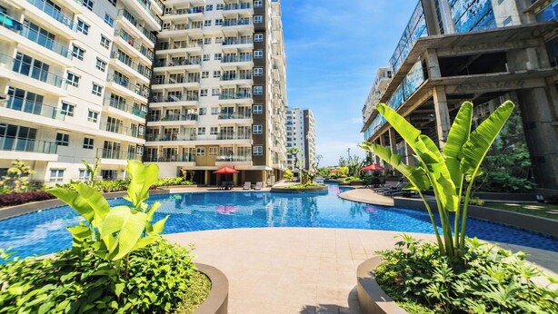 Una piscina rodeada de modernos edificios de apartamentos, con abundante vegetación y zonas de estar al aire libre.