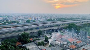 An aerial view of a cityscape with multiple highways, a mix of residential and commercial buildings, and a sunset in the background. - Warm Studio With City View At Lrt City Bekasi Apartment (Bekasi)