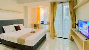A hotel room with a large bed, a desk with a laptop, a TV, and a window with curtains. - Warm Studio With City View At Lrt City Bekasi Apartment (Bekasi)