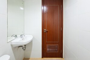 A bathroom with a white sink, a mirror, and a wooden door. - Studio Apartment Near Bojong Indah Station At Vittoria Residence (Jakarta)