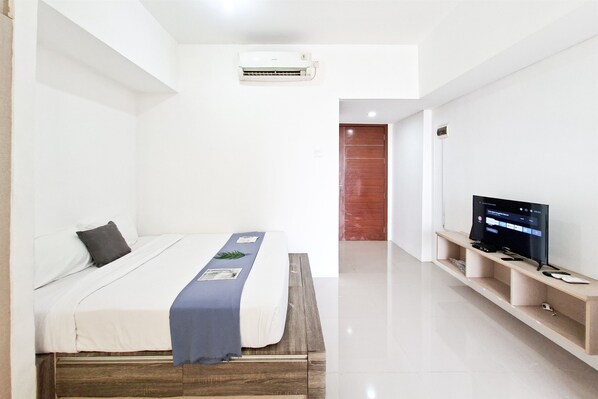 A modern hotel room with a bed, a TV, and a wooden bench. - Studio Apartment Near Bojong Indah Station At Vittoria Residence (Jakarta)