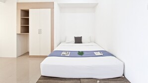 Una habitación compacta con cama, armario y un pequeño rincón de descanso.