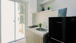 A modern kitchen with a black refrigerator, a gas stove, and a sink. There is a sliding glass door leading to a balcony. - Good Choice 2Br Apartment Near Krl Station At Vittoria Residence (Jakarta)