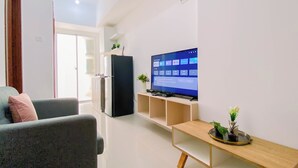 A modern living room with a flat-screen TV, a refrigerator, and a wooden coffee table. - Good Choice 2Br Apartment Near Krl Station At Vittoria Residence (Jakarta)