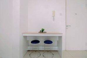 A room with a white door, a small shelf with a plant, and two blue chairs. - Compact With Minimalist Designed 2Br At Bassura City Apartment (Jakarta)