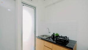 A modern kitchen with a black countertop, wooden cabinets, a stainless steel sink, and a small potted plant. - Compact With Minimalist Designed 2Br At Bassura City Apartment (Jakarta)