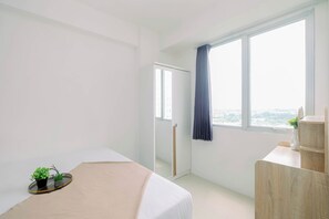 A modern hotel room with a bed, a small table with plants, a wardrobe, and a large window with a view. - Compact With Minimalist Designed 2Br At Bassura City Apartment (Jakarta)