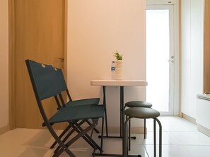 Una habitación pequeña con una puerta de madera, una pared blanca, una mesa con una planta y una botella de agua, una silla azul y un taburete.