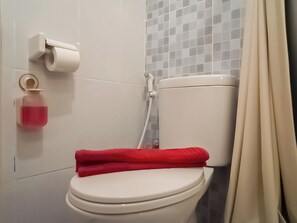Inodoro blanco con una toalla roja encima, un dispensador de papel higiénico y un dispensador de jabón.