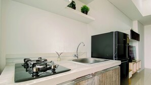 A modern kitchen with a gas stove, a sink, and a black refrigerator. - Nice Look 2Br Apartment At Vittoria Residence (Jakarta)