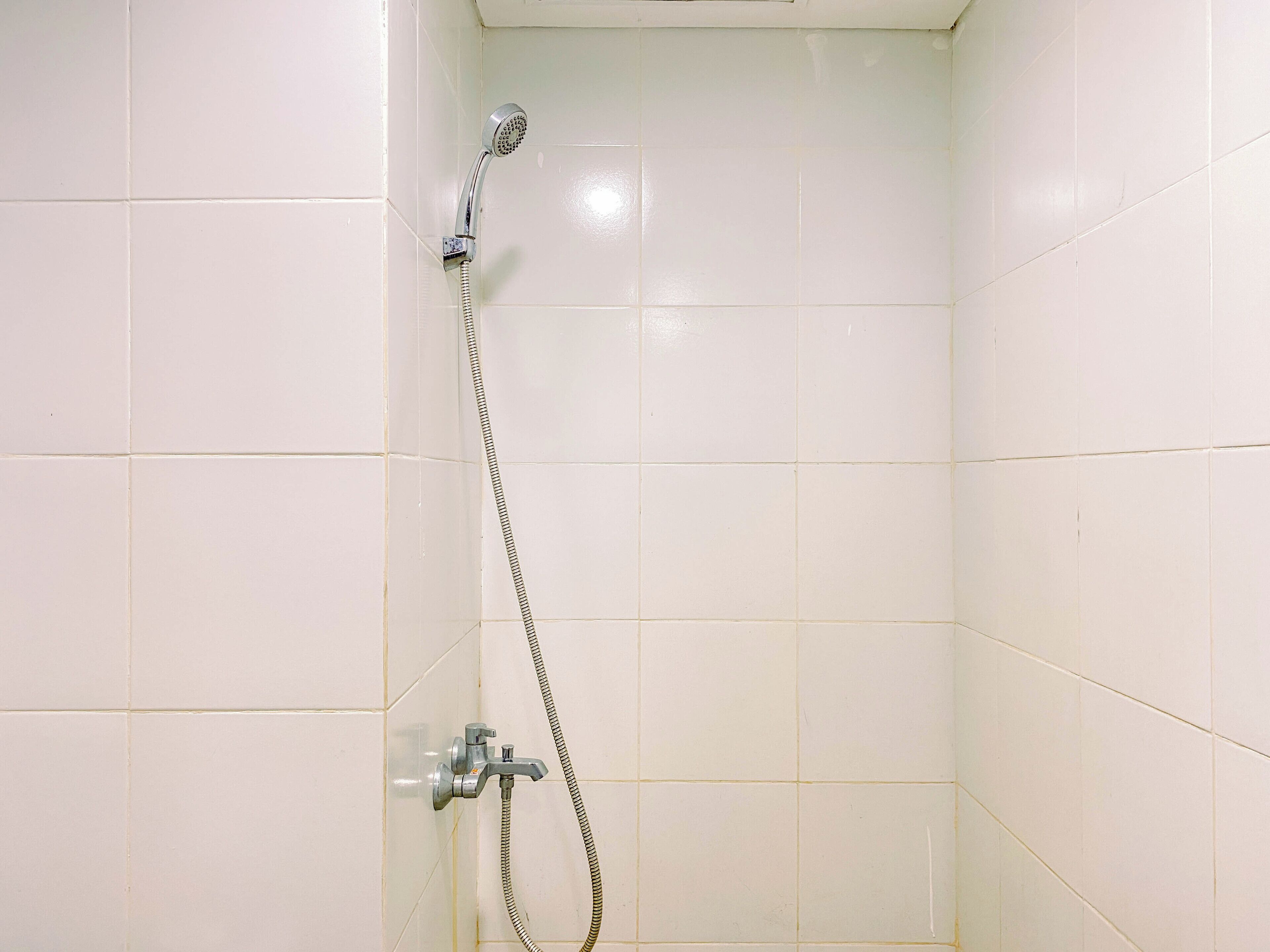 Ein kleiner Duschbereich mit Fliesen, einer Handbrause und einem fest installierten Wasserhahn.