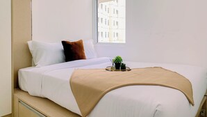 Ein ordentlich bezogenes Bett mit weißer und brauner Bettwäsche, ein kleiner Blumentopf auf einem Nachttisch und ein Fenster mit Blick auf Gebäude.