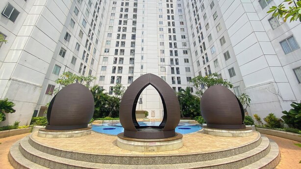 A modern building with a central courtyard featuring a unique sculpture and a pool. - Serene And Warm 2Br At Apartment Bassura City (Jakarta)