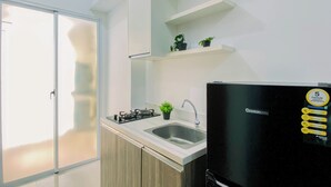 A modern kitchen with a gas stove, sink, and black refrigerator. There is a sliding glass door leading to a balcony. - Compact White 2Br Near Rawa Buaya Station At Vittoria Residence (Jakarta)