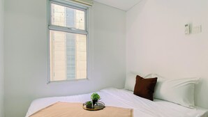 A bedroom with a single bed, a window, and a thermostat on the wall. - Compact White 2Br Near Rawa Buaya Station At Vittoria Residence (Jakarta)