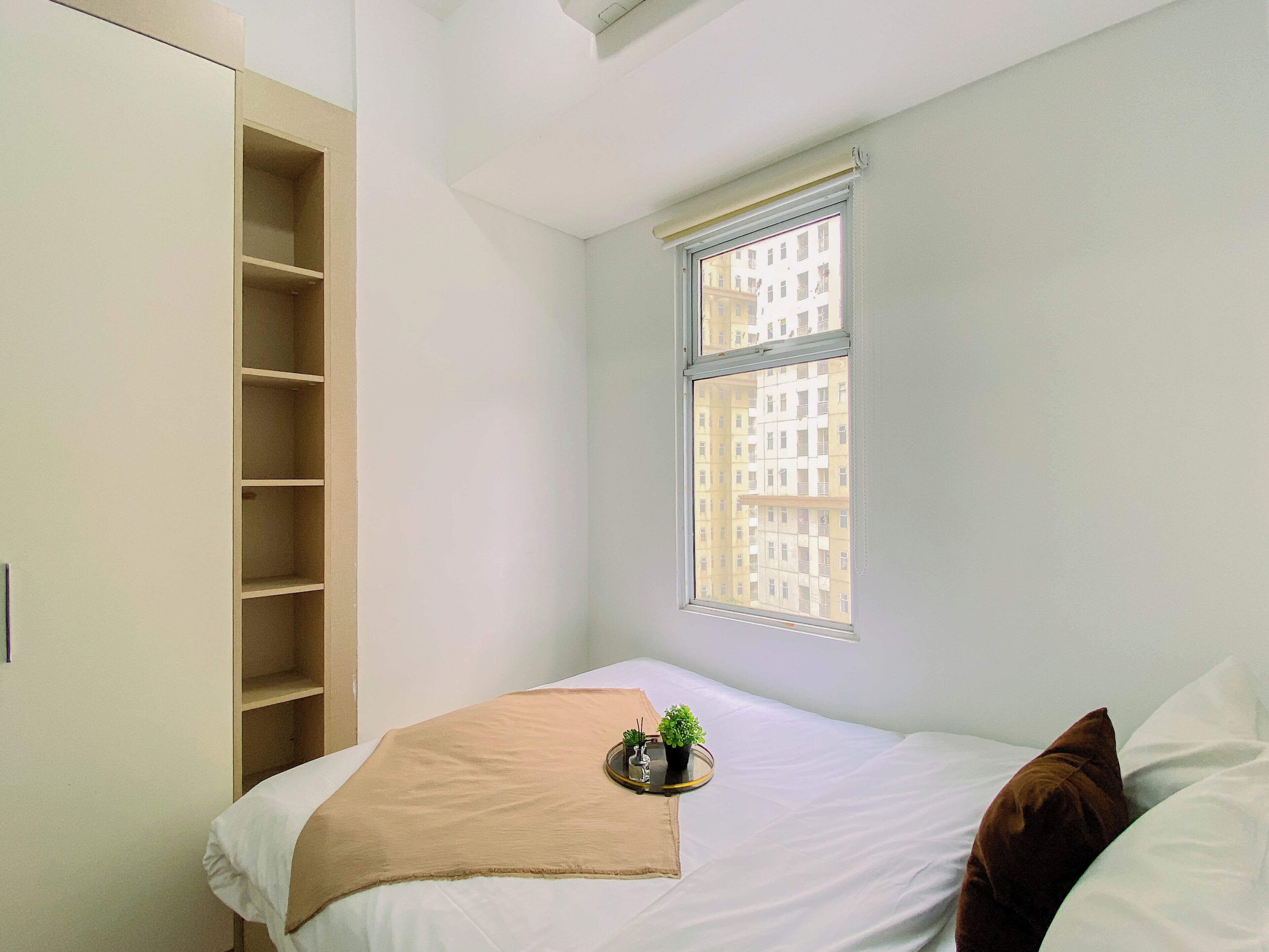A bedroom with a bed, a window with a view of buildings, and a wardrobe.