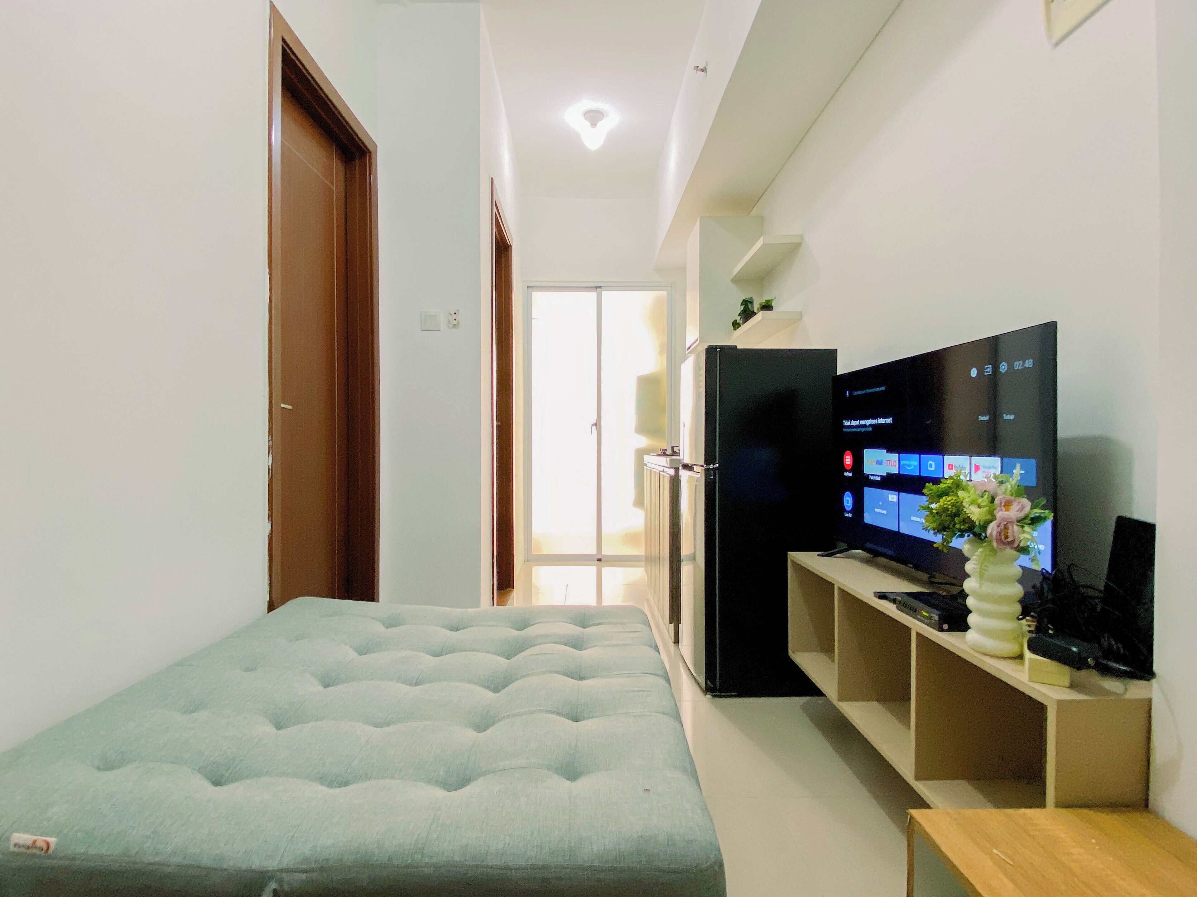 A modern living room with a sofa, a flat-screen TV, a refrigerator, and a small plant on a shelf.