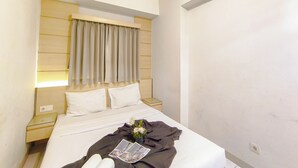 Habitación de hotel con cama, mesita de noche, cortinas en una ventana y lámpara fijada a la pared.